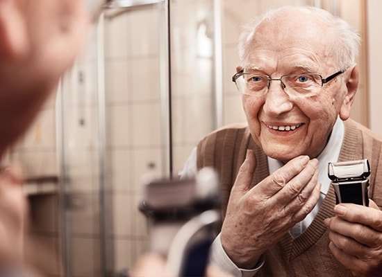 starszy mężczyzna z maszynką do golenia przed lustrem